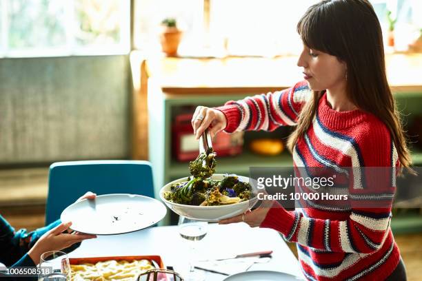 young hispanic woman in striped sweater serving food from bowl - serving dish foto e immagini stock