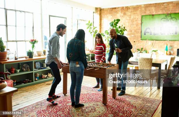 Four friends playing table football and drinking in modern hip apartment