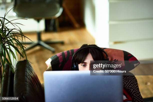 woman using laptop and wearing headphones - couch laptop stock-fotos und bilder