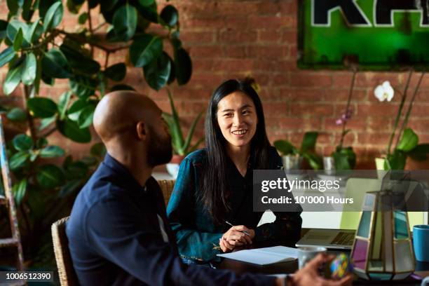 mid adult asian woman smiling towards male colleague - studio interview stockfoto's en -beelden