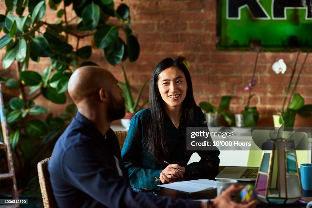Mid adult Asian woman smiling towards male colleague