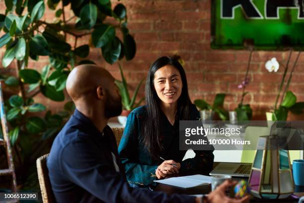 mid adult asian woman smiling towards male colleague - interview imagens e fotografias de stock