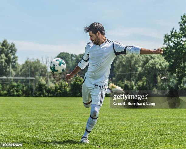 soccer player kicking ball on pitch - fußballspieler stock-fotos und bilder