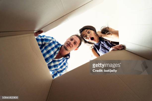 two young people looking surprised into a carton box - damaged box stock pictures, royalty-free photos & images