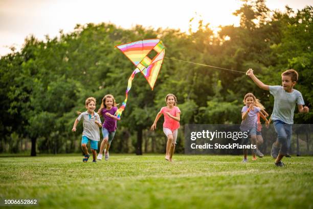glückliche kinder laufen für ein fliegender drache - kite toy stock-fotos und bilder