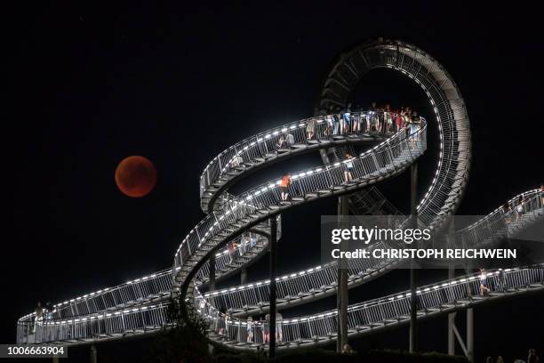 The full moon can be seen behind the landmark "Tiger and Turtle" sculpture and walkway during a "blood moon" eclipse over Duisburg, western Germany,...