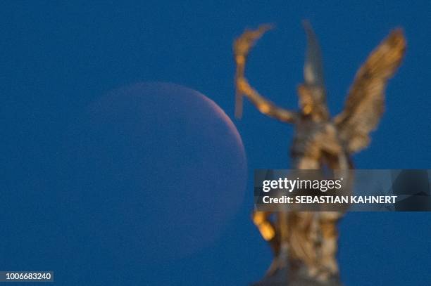 The full moon appears behind a golden angel statue on the roof of the Academy of Fine Arts during a "blood moon" eclipse over Dresden, eastern...