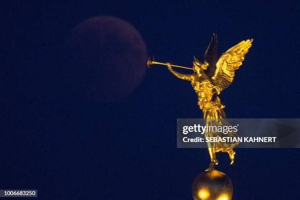 The full moon appears behind a golden trumpet angel statue during a "blood moon" eclipse over Dresden, eastern Germany, on July 27, 2018. - The...