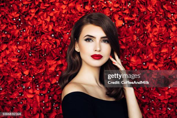 portrait of a beautiful woman standing against floral pattern - woman with red lipstick stock pictures, royalty-free photos & images