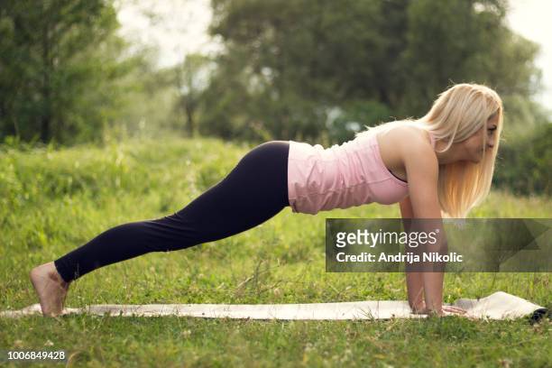 giovane donna che fa tavola su un campo erboso - blonde yoga foto e immagini stock