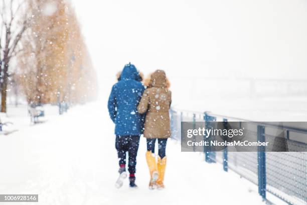 rear view of couple walking away in snow storm defocused version - winter jacket stock pictures, royalty-free photos & images