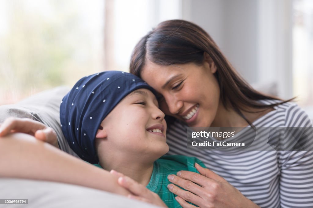An elementary-age boy battling cancer sits with his mother on the couch