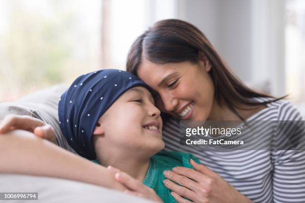 en elementär-ålder boy slåss cancer sitter med sin mor på soffan - cancer illness bildbanksfoton och bilder