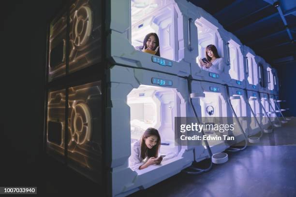 three asian chinese female tourist check in capsule hotel room and surfing internet and selfie on their bed with their mobile phone while one of them reading from her notebook