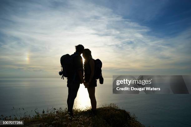 hiking couple looking out to sea silhouette on atlantic coastline. - gap year stock pictures, royalty-free photos & images