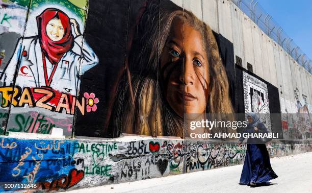 Palestinian woman walks past a mural painted on Israel's controversial separation barrier in the West Bank city of Bethlehem on July 29 drawn by...