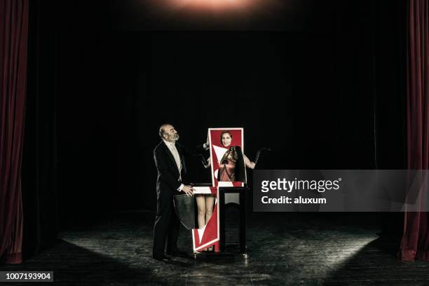 magician performing trick with his assistant who is cut in half in the magic box - magician stock pictures, royalty-free photos & images