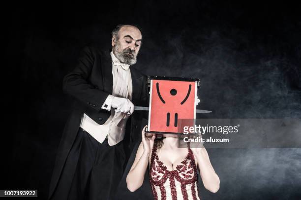 magician performance magician assistant with head inside box with magician inserting swords - tail coat stock pictures, royalty-free photos & images