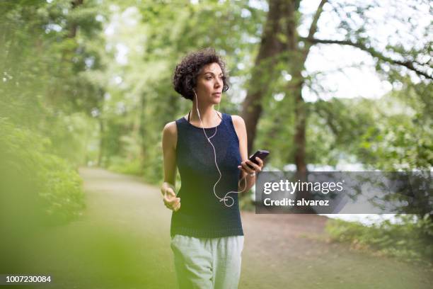 vrouw luisteren naar muziek tijdens het wandelen in het bos - walking stockfoto's en -beelden