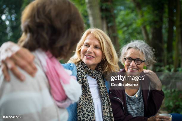 woman sitting arms around friends at lakeshore - mature women group stock pictures, royalty-free photos & images