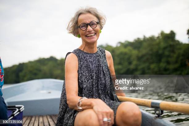lächelnde reife frau sitzen auf ruderboot im see - middle aged woman stock-fotos und bilder