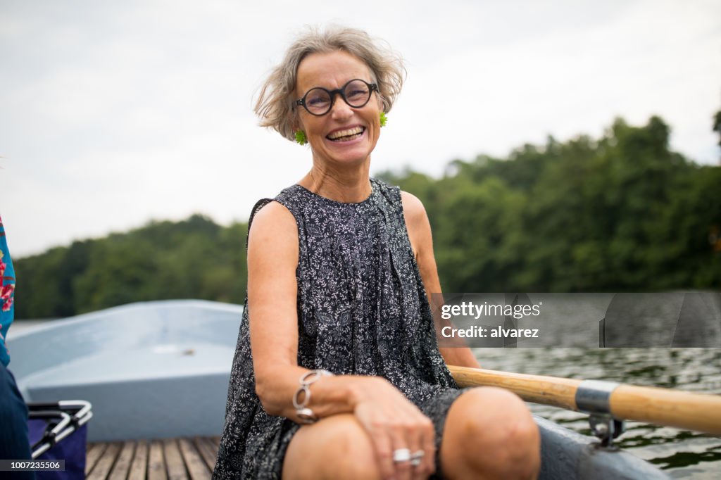 Mulher madura sorridente, sentado no barco a remo no lago