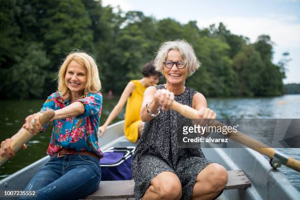 sorridenti amiche canottaggio in lago - group adventure foto e immagini stock