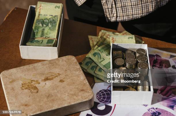 Bundles of Zimbabwean two dollar bond banknotes and a box of coins sit on a table in Bindura, Zimbabwe on Sunday, July 29, 2018. Zimbabweans will...