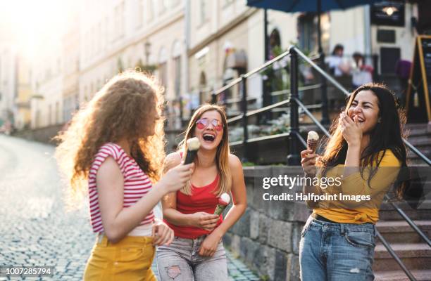 three cheerful female teenager friends with ice cream standing on the street, laughing. - slovakia town stock pictures, royalty-free photos & images