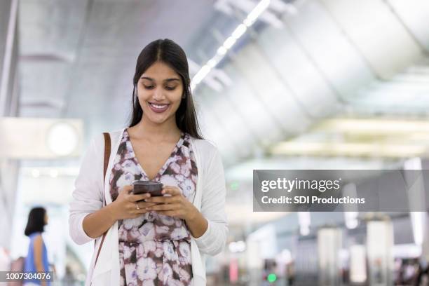 young woman texts friend from airport terminal - singapore airport stock pictures, royalty-free photos & images