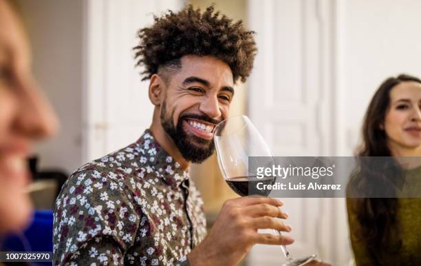 smiling man drinking red wine during dinner party at home - afro friends home stock pictures, royalty-free photos & images