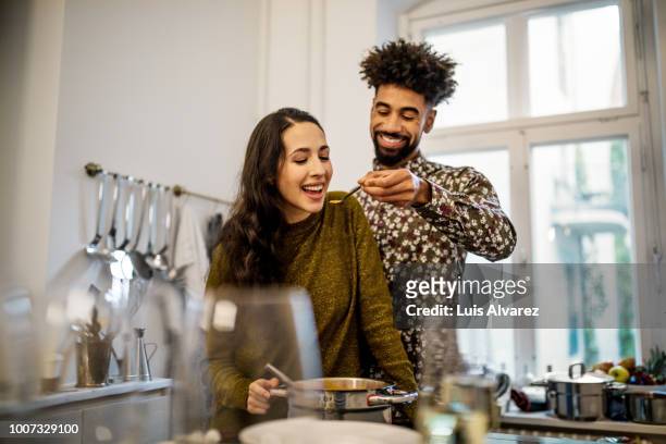 man feeding pumpkin soup to girlfriend in kitchen - cooking together stockfoto's en -beelden