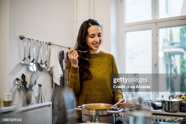 woman tasting freshly made squash soup in kitchen - soup home foto e immagini stock