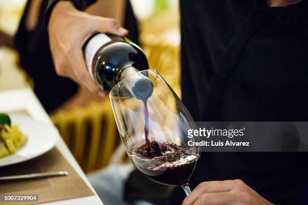 man pouring red wine in glass during dinner party - red wine glass stock-fotos und bilder