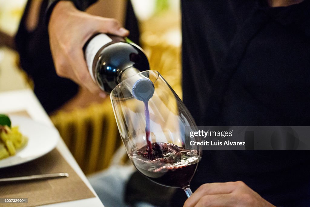 Man pouring red wine in glass during dinner party