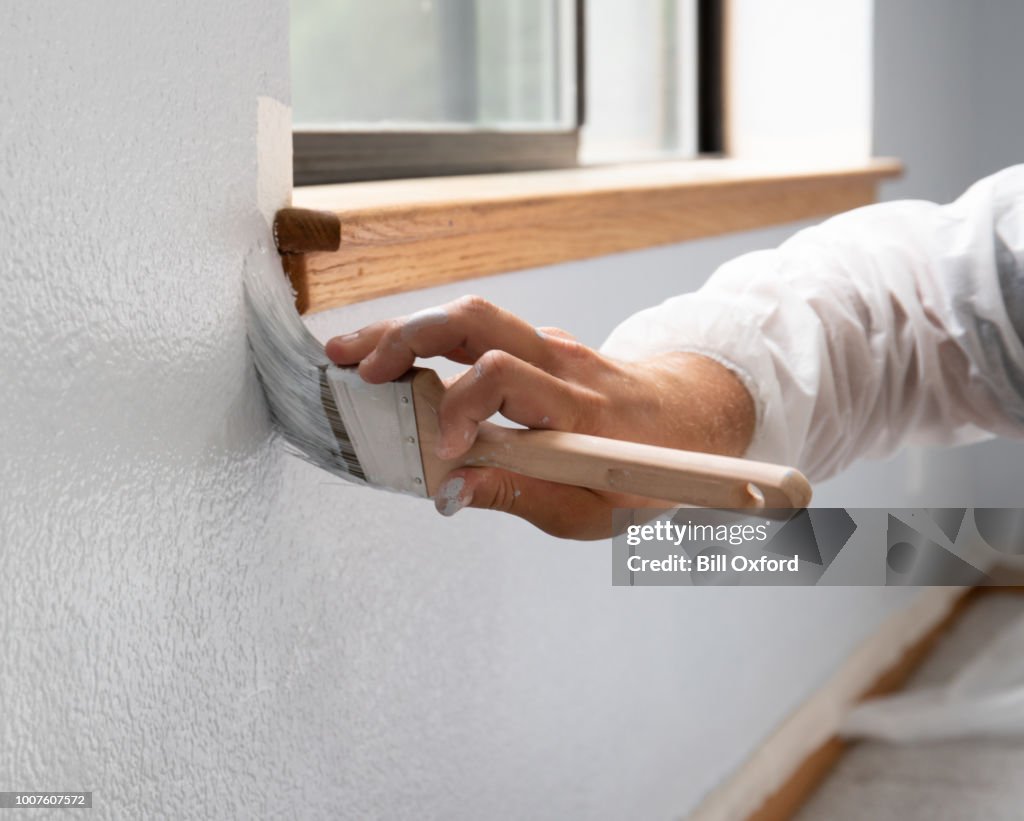Man painting interior of home by window