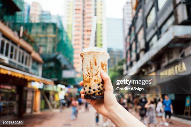 human hand holding a bottle of iced cold bubble tea against city street in a hot summer day - fashion hong kong stock-fotos und bilder