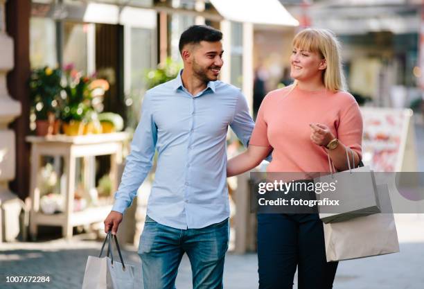 einkaufen: glückliche paar mit einkaufstüten spaziergänge durch straßen - chubby man shopping stock-fotos und bilder