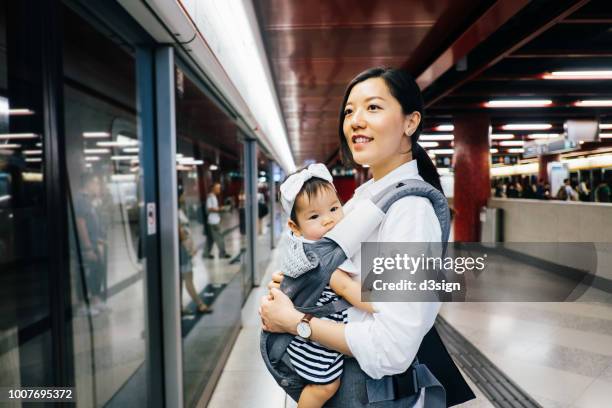 young mother carrying cute baby girl waiting for subway in subway station - carrying sign ストックフォトと画像