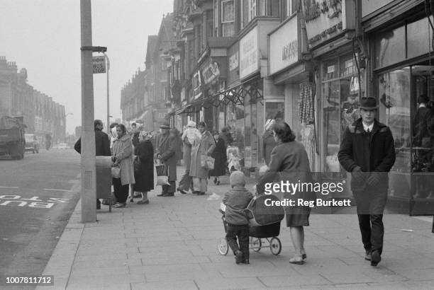View of shoppers and residents, including recent migrants from Commonwealth countries, queuing at a bus stop on a shopping street in the town of...