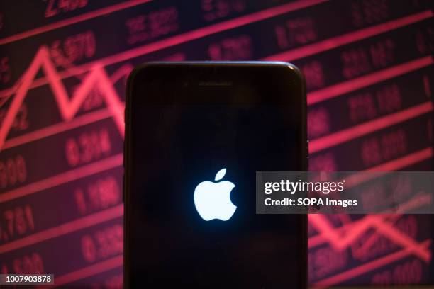 In this photo illustration, an iPhone displays the Apple logo with a background of a market value dropping on the stock exchange behind.