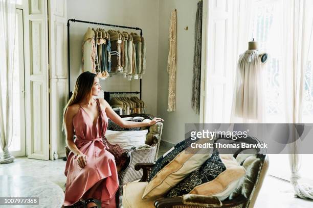 woman sitting in boutique admiring dress on mannequin in window - vestito da donna foto e immagini stock