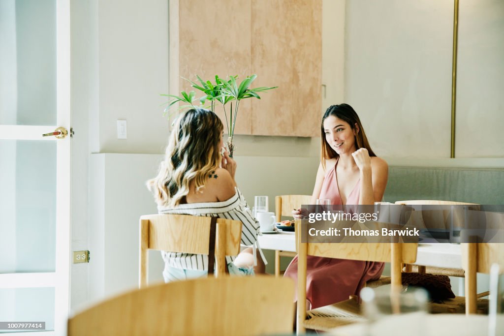 Smiling female friends in discussion while sharing food in restaurant
