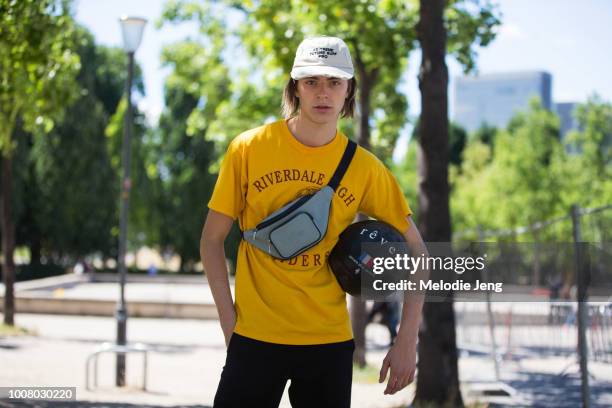 Model Pierre Podevyn wears a white "Extreme Future Surf Pro" ca, gray cross-body Lacoste fanny pack, yellow Riverdale high school t-shirt, and black...