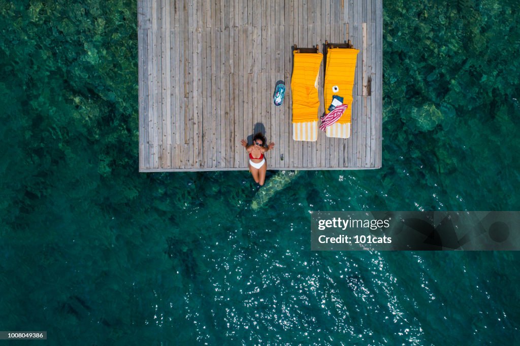 Beautiful woman sunbathing alone on a wooden pier in sea aerial photo