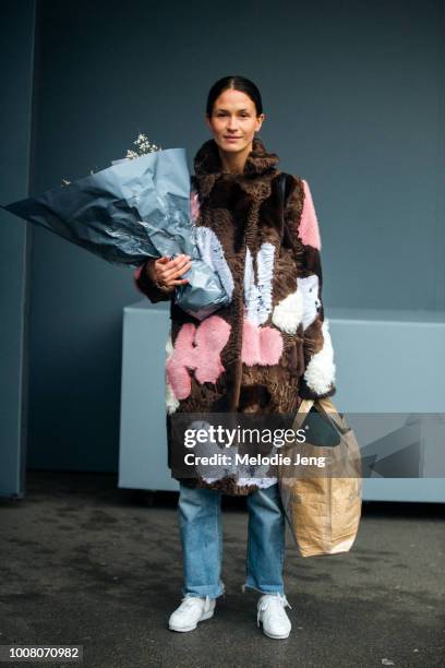 Model Emma Leth wears a brown floral fur coat, Comme des Garcons brown shopping bag, blue jeans, white sneakers, and a flower bouquet from Moulie...