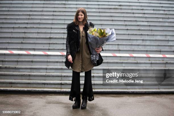 Model Jennae Quisenberry in a black shearling bomber jacket, green top, black flare pants, black boots, and a bouquet of flowers from Moulie Fleurs...