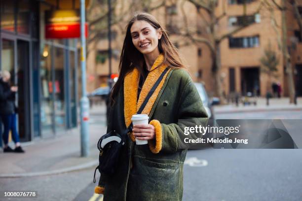 Model Marine Deleeuw wears a green shearling leather jacket and holds a Starbucks coffee cup on Day 3 of the London Fashion Week February 2017...