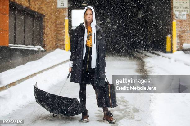 Model Kristy Kaurova wears a black parka, black purse, white hoodie, black umbrella in the snow on Day 1 of New York Fashion Week Fall/Winter 2017 on...