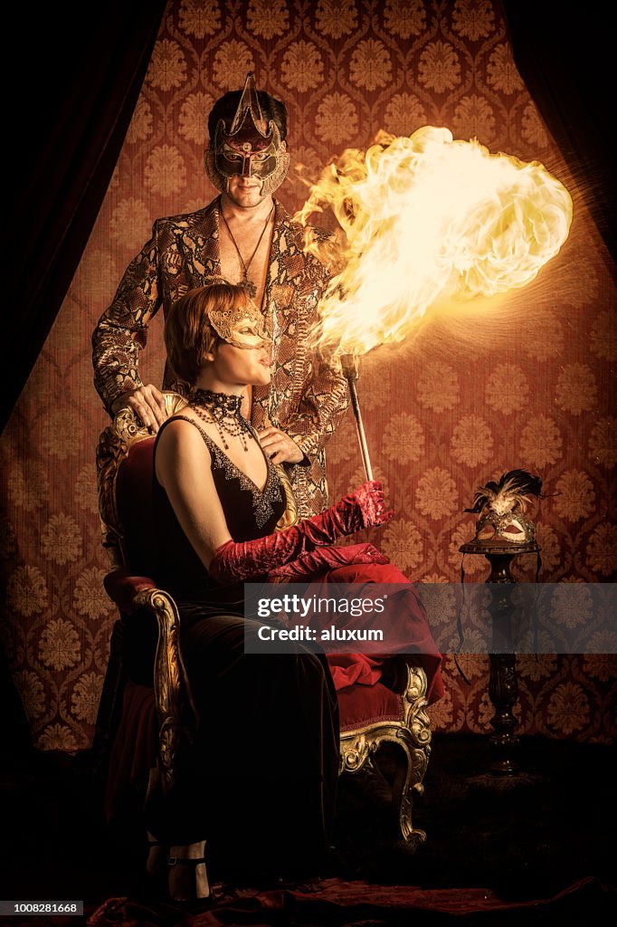 Hombre y mujer usando máscaras venecianas y escupiendo fuego